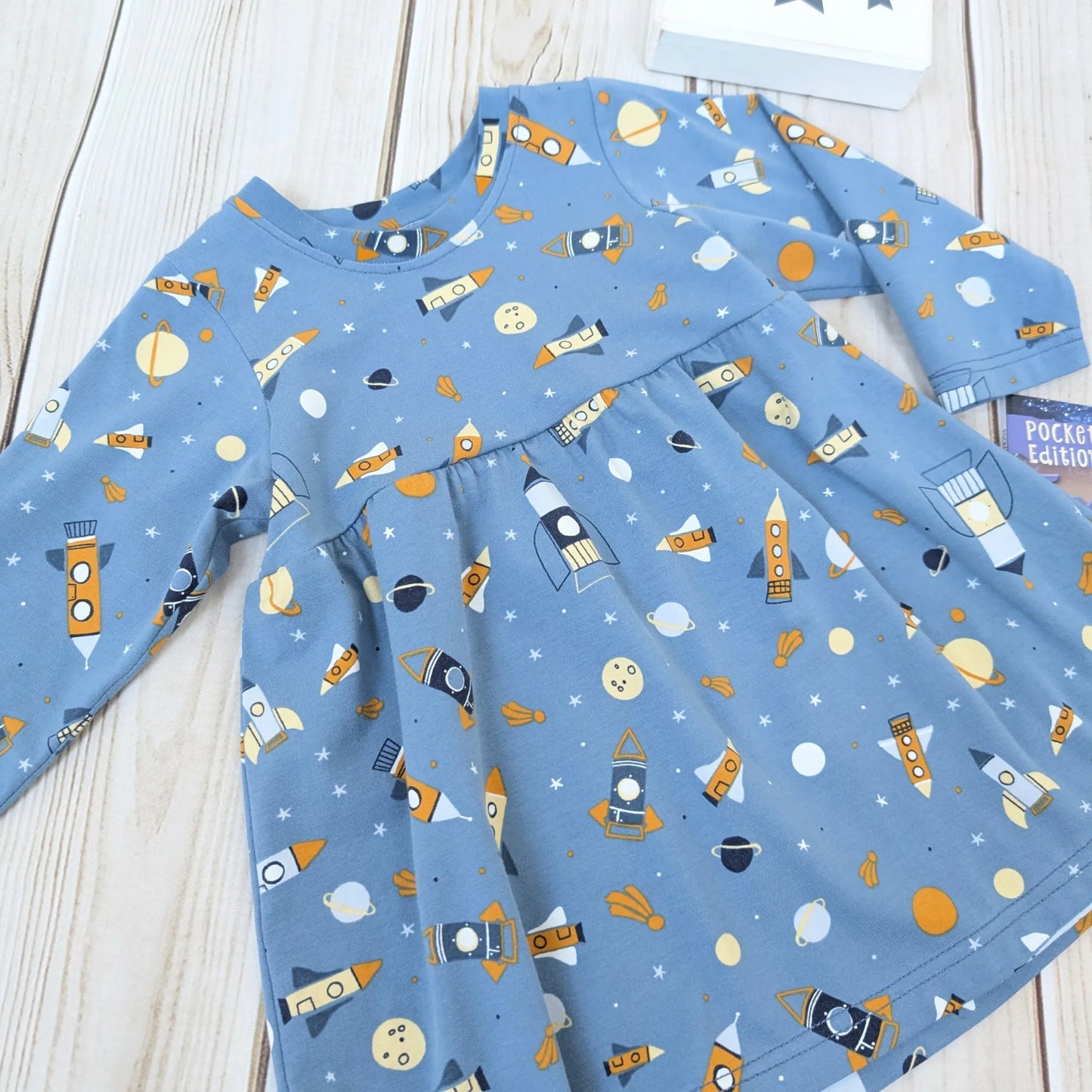 Children's gathered dress with space-themed print on a wooden surface