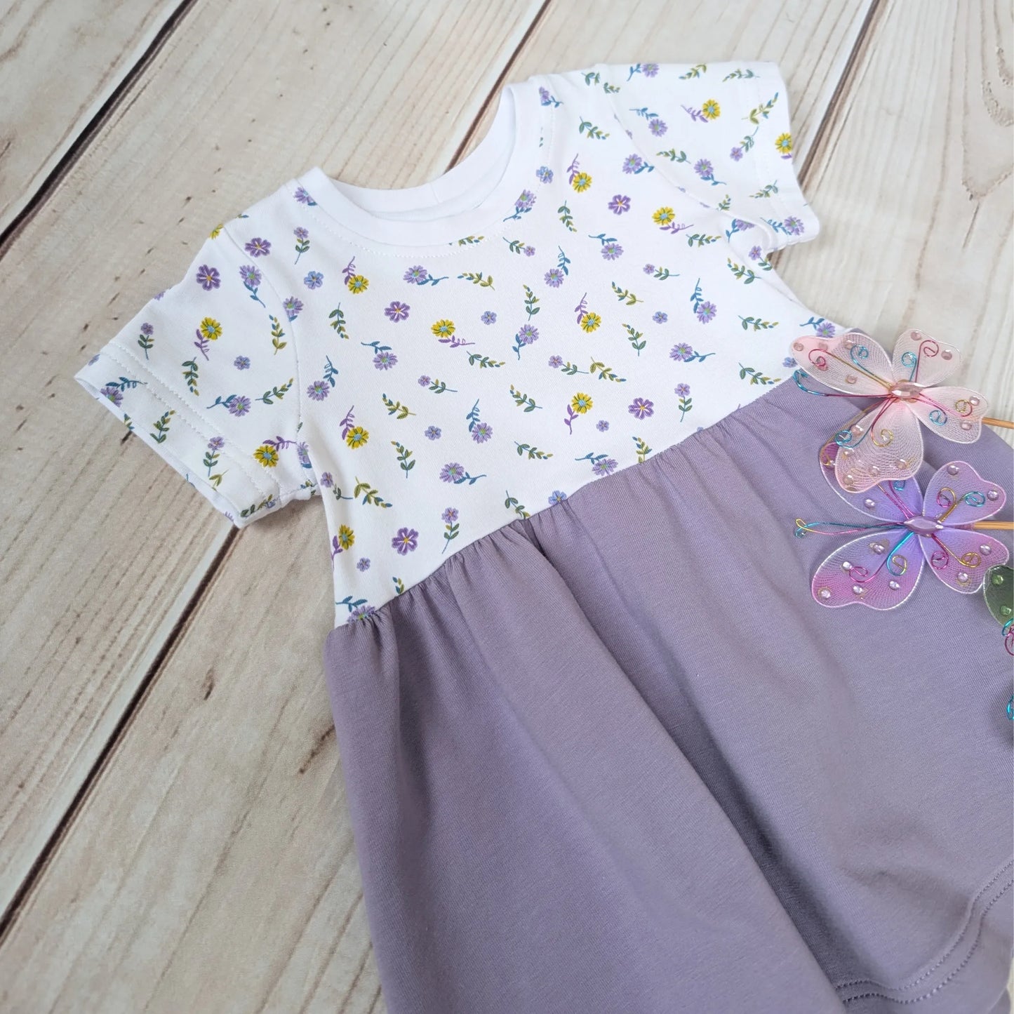 Children's dress with floral top and purple skirt on a wooden surface