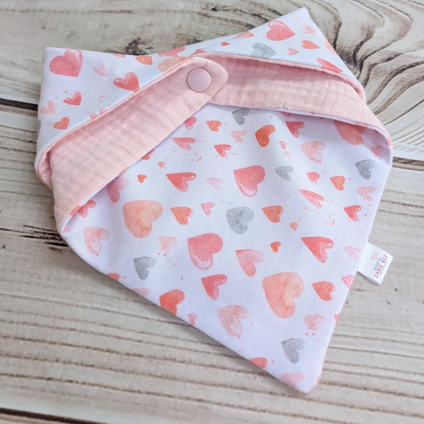 Baby bib folded with heart pattern on a wooden surface