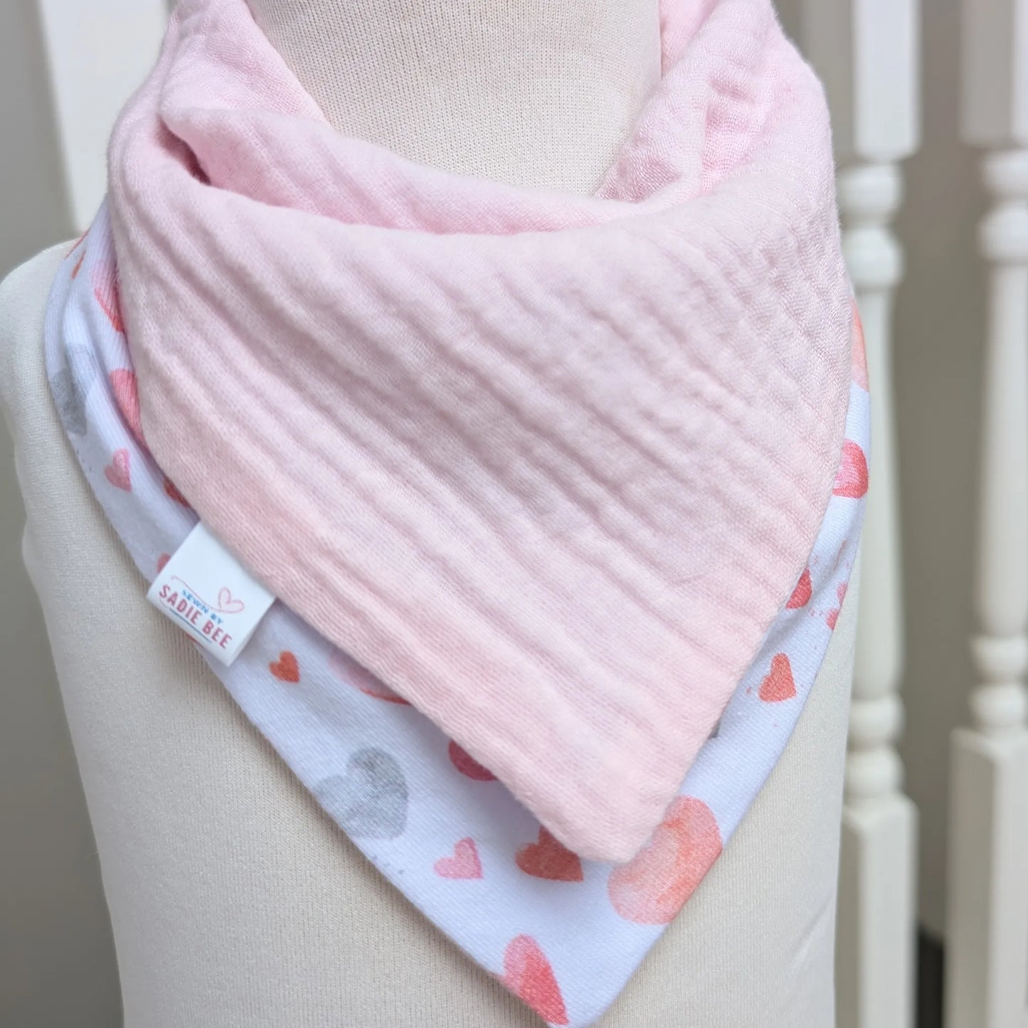 Pink baby bib with heart patterns on a mannequin against a neutral background