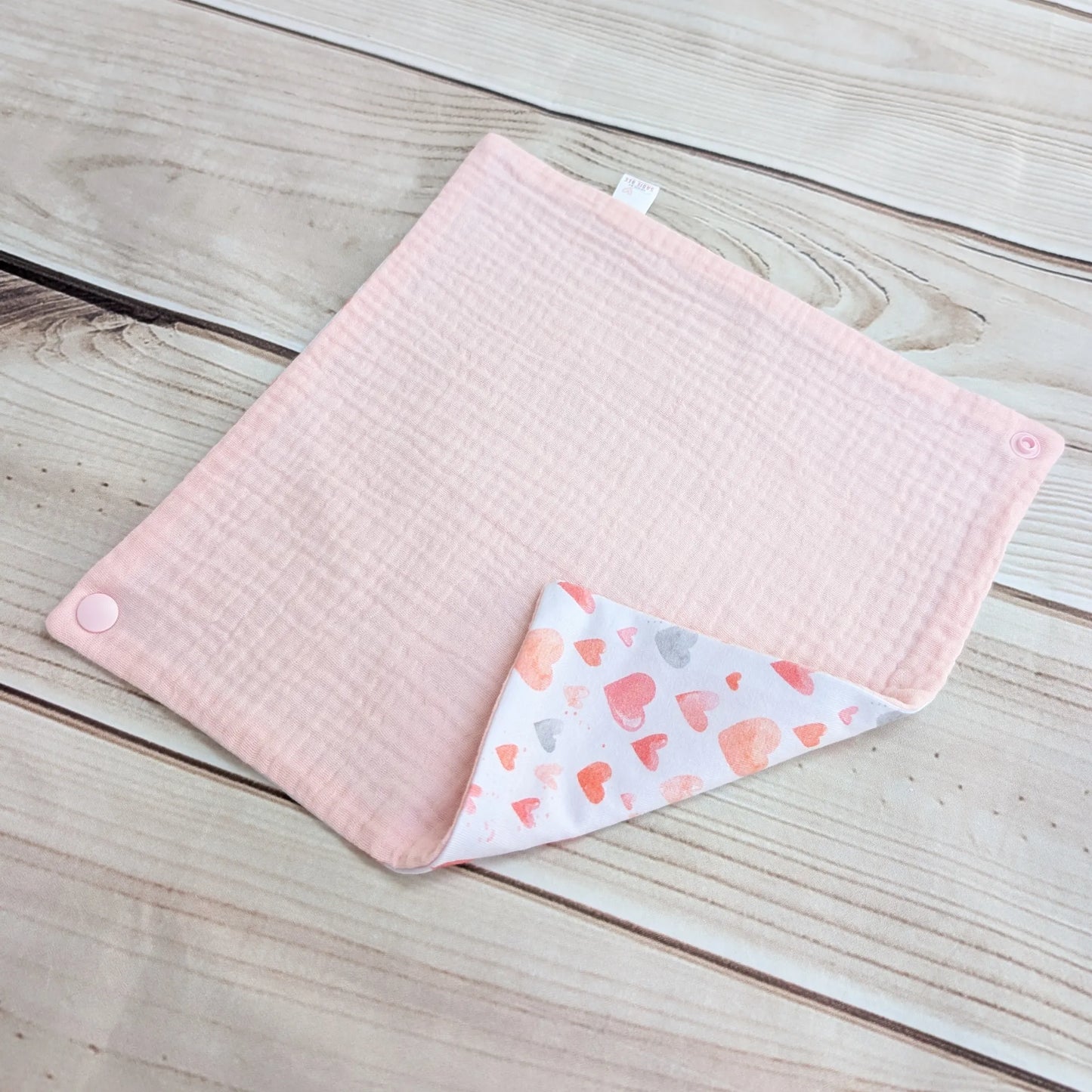 Pink & hearts pattern bib laid out flat on a wooden surface