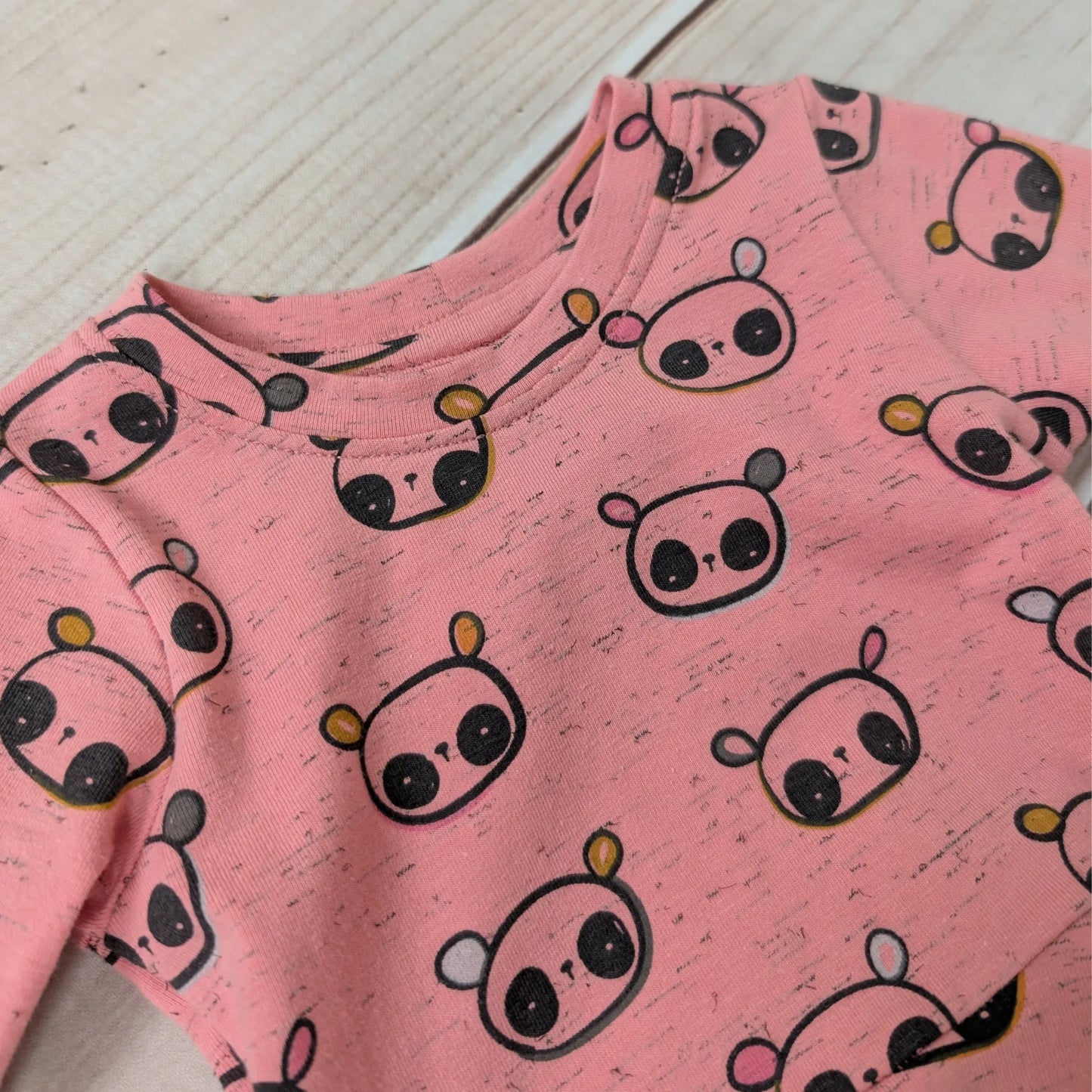 Pink long-sleeve dress close up of neckline with panda pattern on a light wooden surface