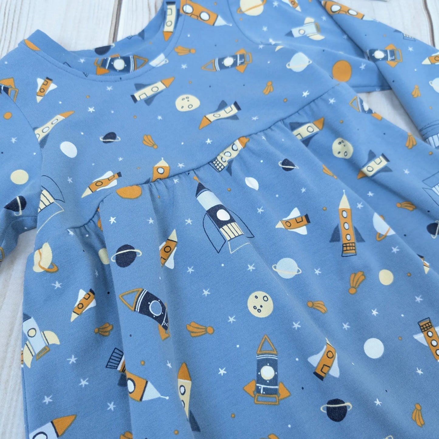 Blue fabric with space-themed pattern including rockets and planets on a wooden surface.