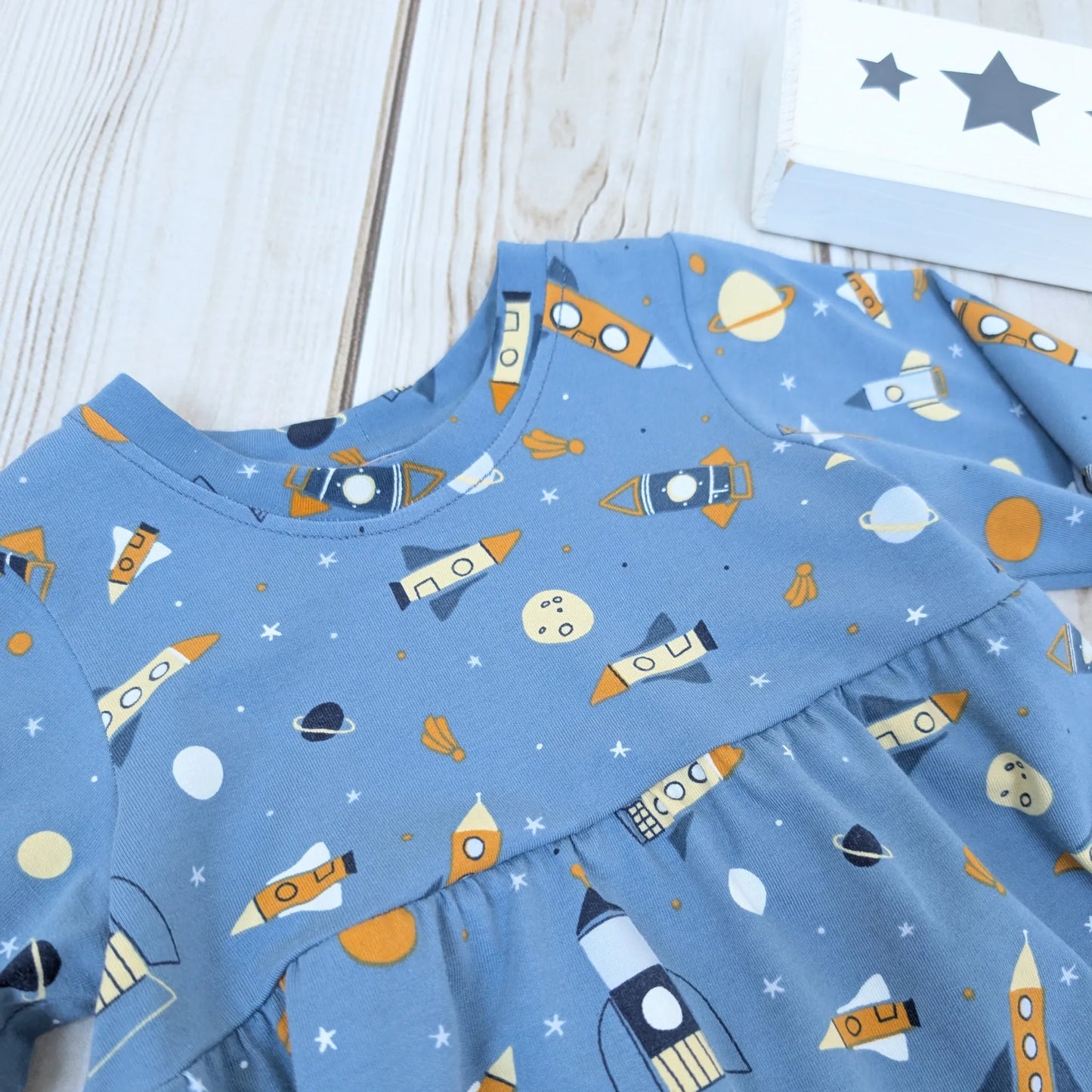 Blue children's dress with space-themed pattern on a wooden surface