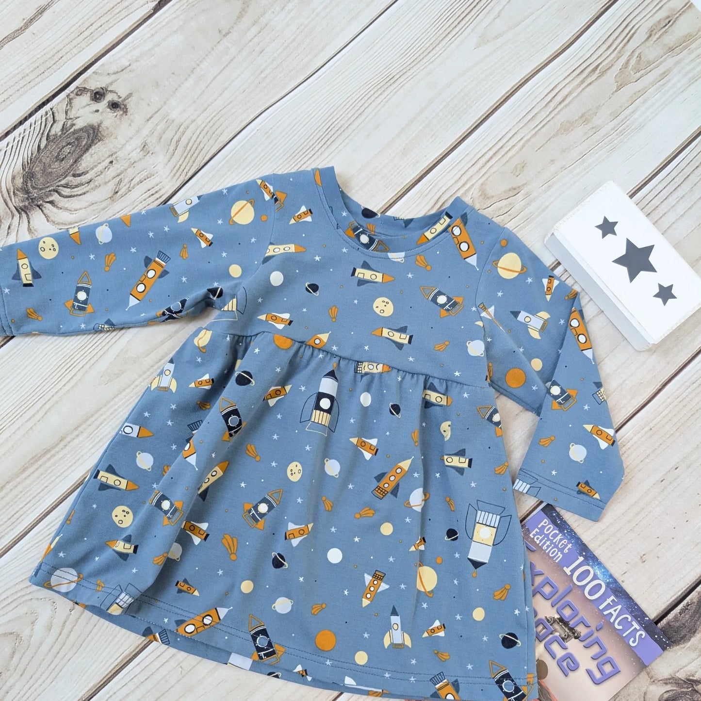 Blue children's dress with space-themed print on a wooden surface