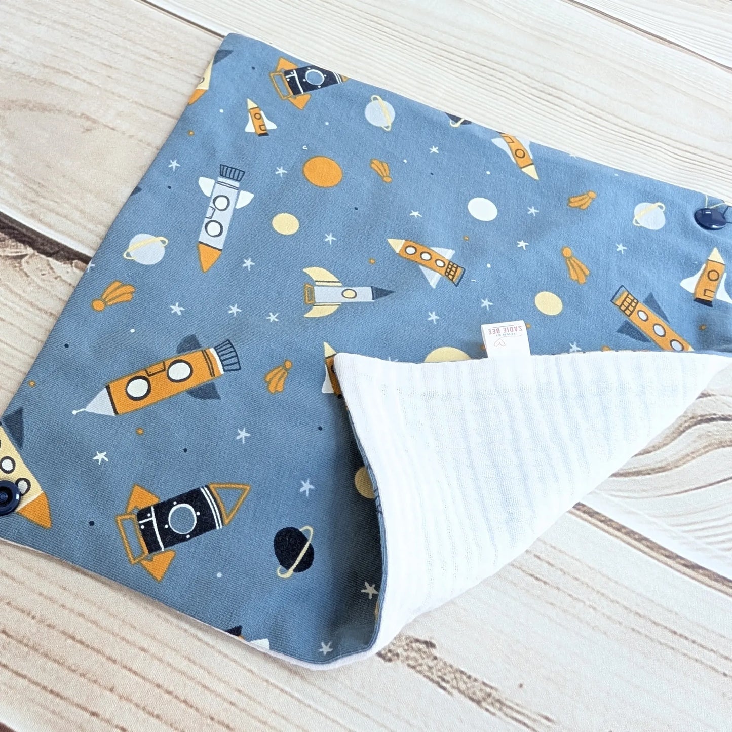 Blue bib foleded out with space-themed pattern on a wooden surface