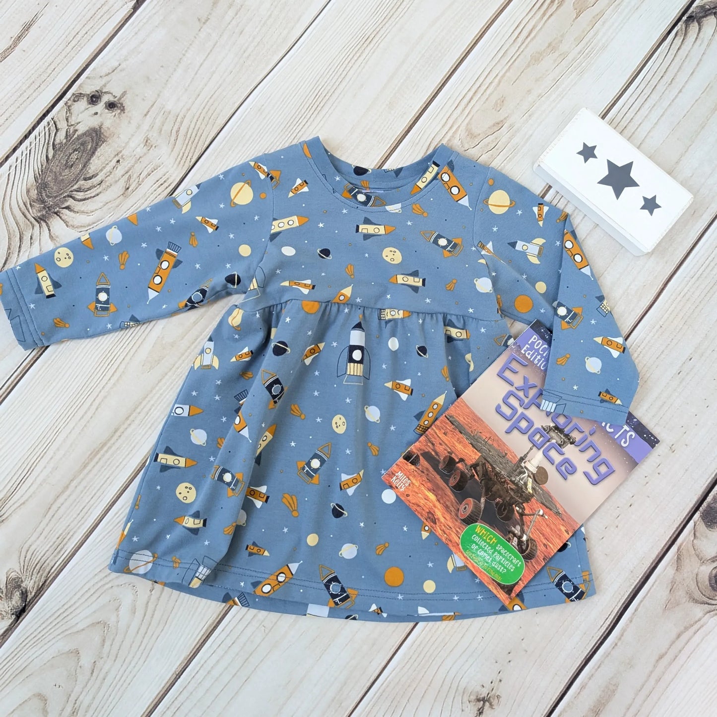 Children's blue long-sleeve skater dress with space-themed print on a wooden surface