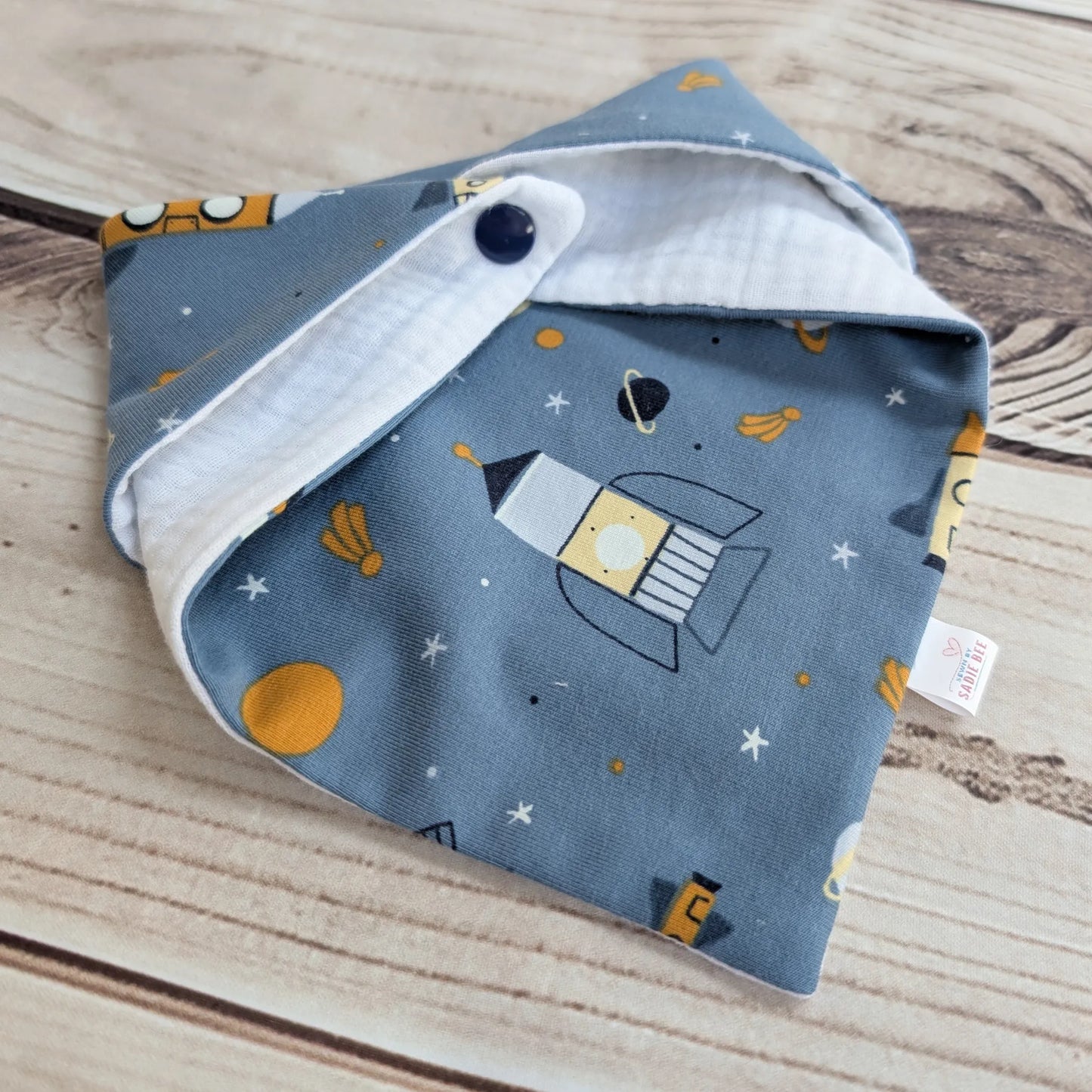 Folded baby drool bib with space-themed design on a wooden surface
