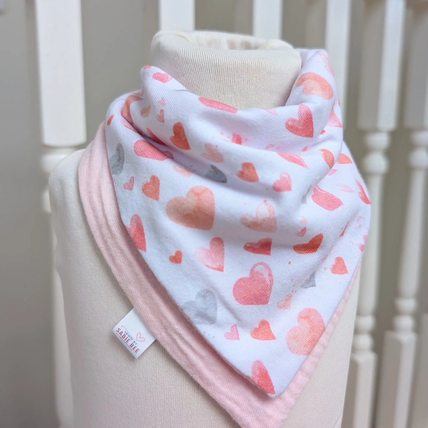Baby bib with heart pattern on a mannequin against a neutral background
