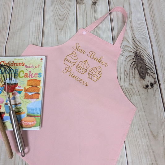 Pink-Handmade-Kids-apron-personalised-text-star-baker-row-of-cupcakes-your-word-choice-book-and-utensils-as-props