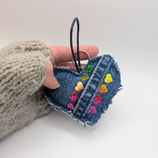 Denim-heart-shaped-keyring-with-two-lines-of-rainbow-hearts-seam-of-jeans-adds-detail-added-loop-and-ring-held-in-my-hand