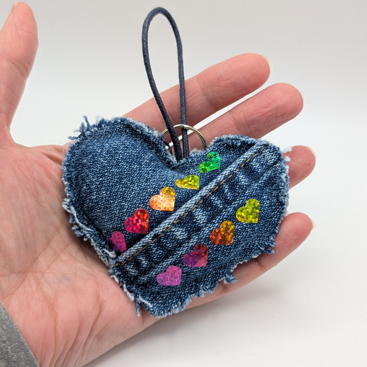 Denim-heart-shaped-keyring-with-two-lines-of-rainbow-hearts-seam-of-jeans-adds-detail-added-loop-and-ring-held-in-my-hand